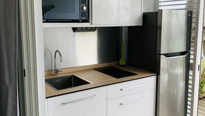 Una cocina compacta con armarios blancos, un refrigerador de acero inoxidable, un microondas y un lavamanos.