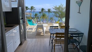 Vista desde un balcón con piso de madera, una mesa con sillas y vista a la playa y al océano.