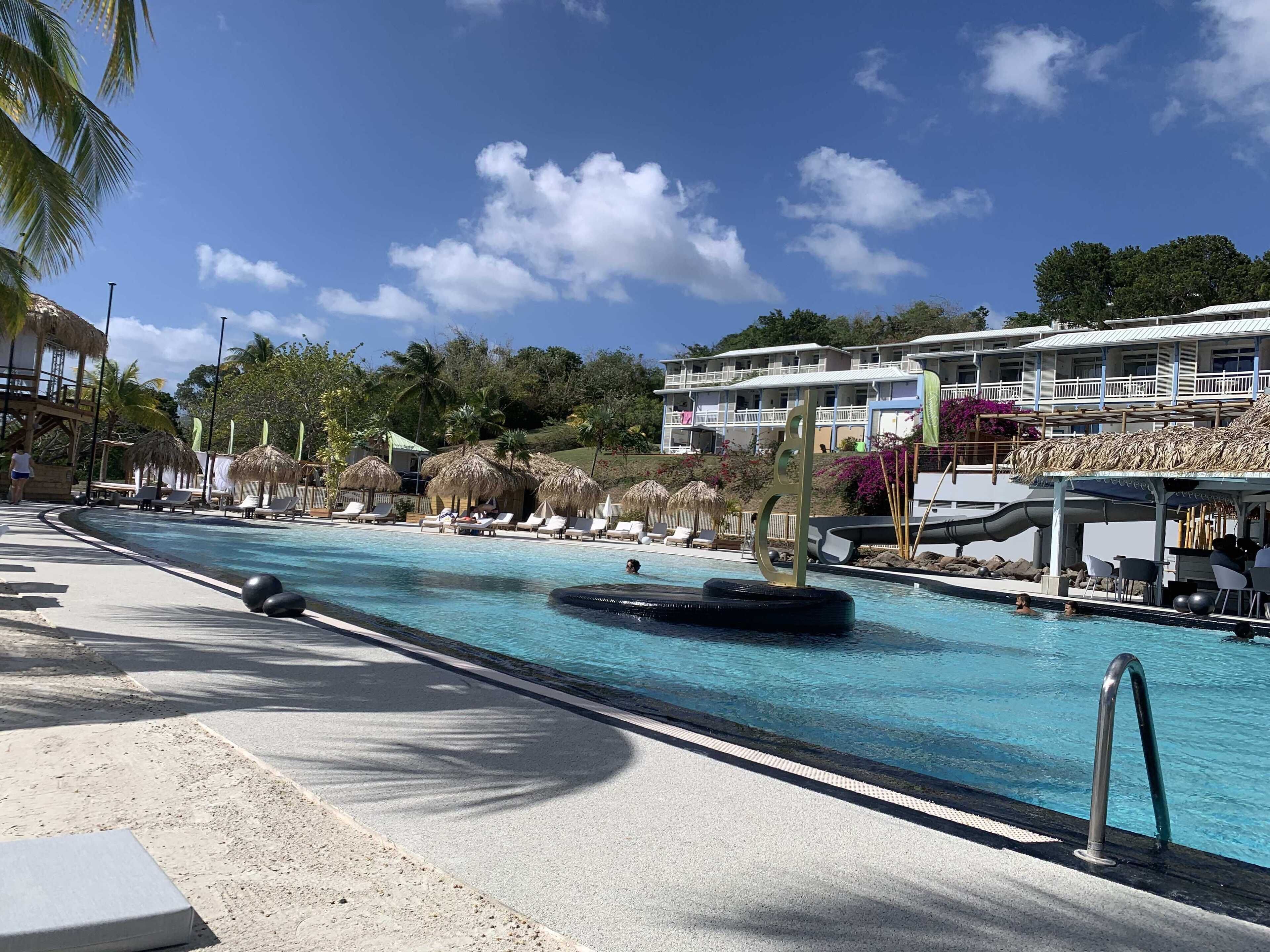 Un área de piscina con sillones de descanso, un tobogán y un edificio con balcones al fondo.