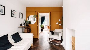 A modern living room with a white sofa, a white armchair, and a coffee table. There is a round mirror on the wall and a plant on the side table. - Modern & Stylish Home in the Heart of Belfast (Belfast)
