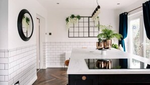 A modern kitchen with a white subway tile backsplash, a black countertop, and a built-in stove. There are potted plants on the counter and a hanging light fixture above. - Modern & Stylish Home in the Heart of Belfast (Belfast)