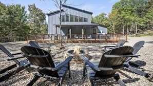 A modern house with a deck, a fire pit, and outdoor seating. - Champagne Pines Escape | Hot Tub + EV | Sleeps 10 (Broken Bow)