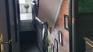 A hallway with a black door, a staircase with a glass railing, and a view into a room with a brick wall and a hanging light fixture. - Stylish Designer 4-Bed Home in the Heart of Belfast (Belfast)