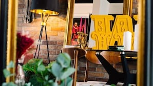 A room with a brick wall, a black floor lamp, a table with a yellow sign, and a mirror reflecting the room. - Stylish Designer 4-Bed Home in the Heart of Belfast (Belfast)