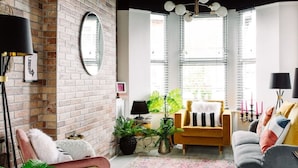 A cozy living room with a brick wall, a round mirror, a yellow armchair, a grey sofa, and a black floor lamp. - Stylish Designer 4-Bed Home in the Heart of Belfast (Belfast)