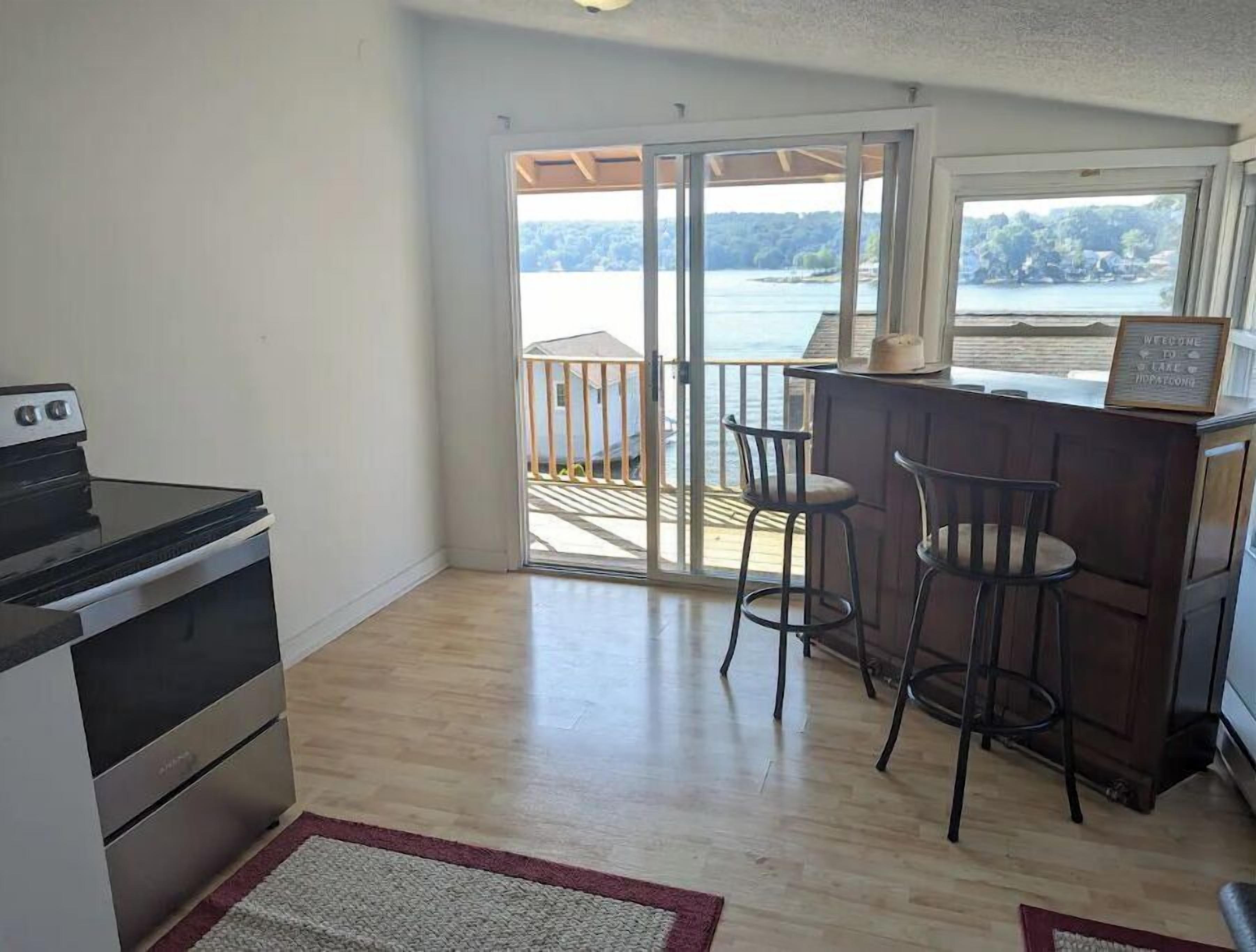 Une cuisine équipée d’une cuisinière, un coin bar avec des tabourets et une porte-fenêtre coulissante donnant sur un balcon avec vue sur un lac.