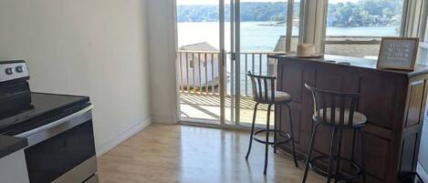 Une cuisine équipée d’une cuisinière, un coin bar avec des tabourets et une porte-fenêtre coulissante donnant sur un balcon avec vue sur un lac.
