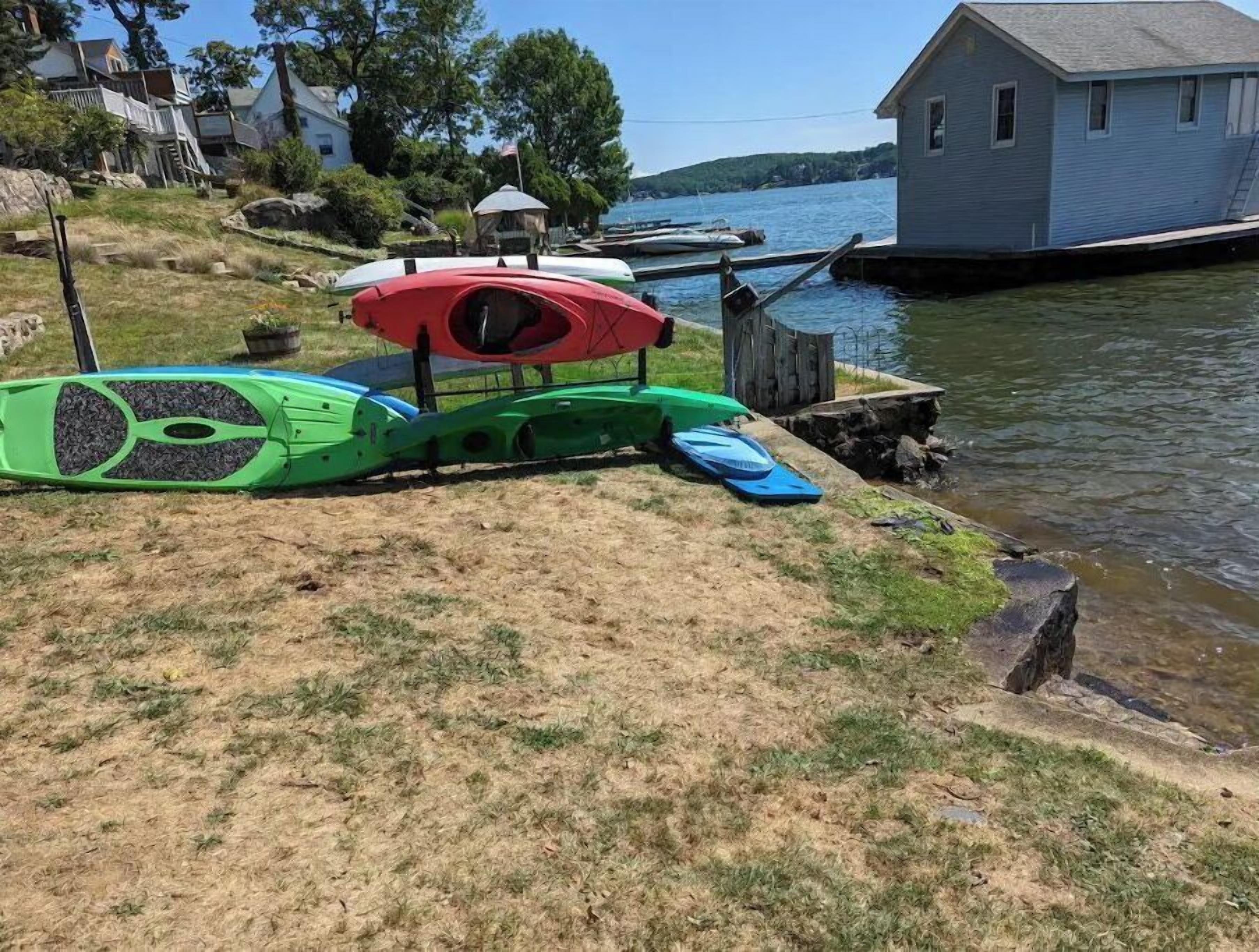 A lakeside property with a dock, a small house, and a grassy area with kayaks and a paddleboard.