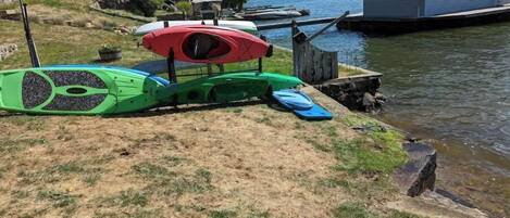 A lakeside property with a dock, a small house, and a grassy area with kayaks and a paddleboard.