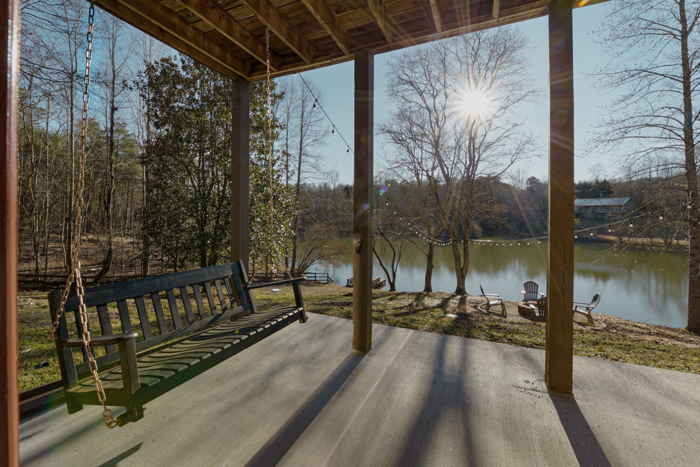 A wooden swing set with a bench, a concrete deck, and a view of a lake with trees and a distant building.