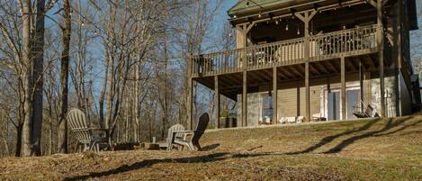 A two-story wooden cabin with a balcony, surrounded by trees.