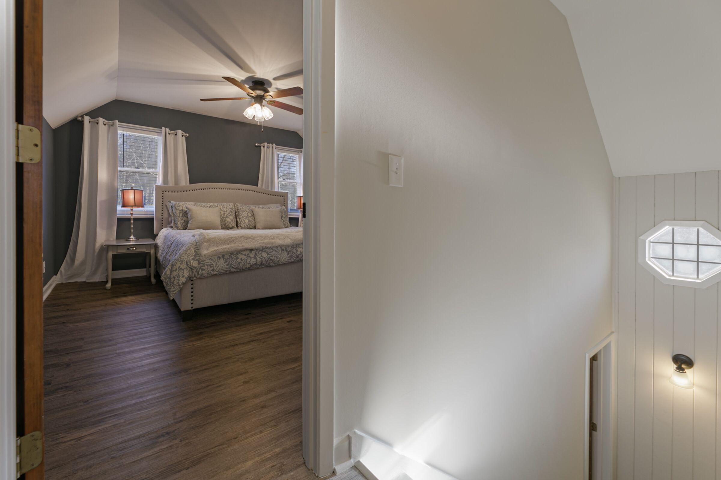 Une chambre à coucher avec un lit, des tables de chevet, un ventilateur de plafond et une fenêtre avec des rideaux.
