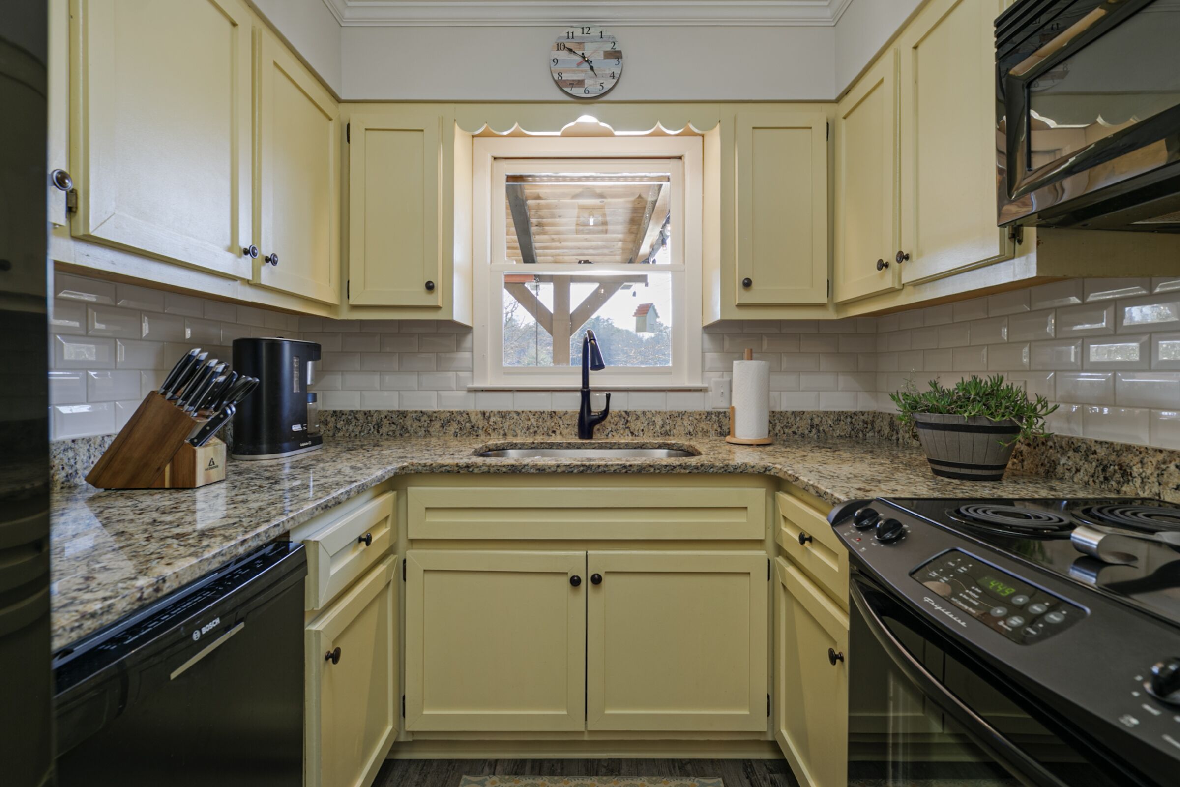 A kitchen with yellow cabinets, a built-in oven, a sink, and a window with a view.