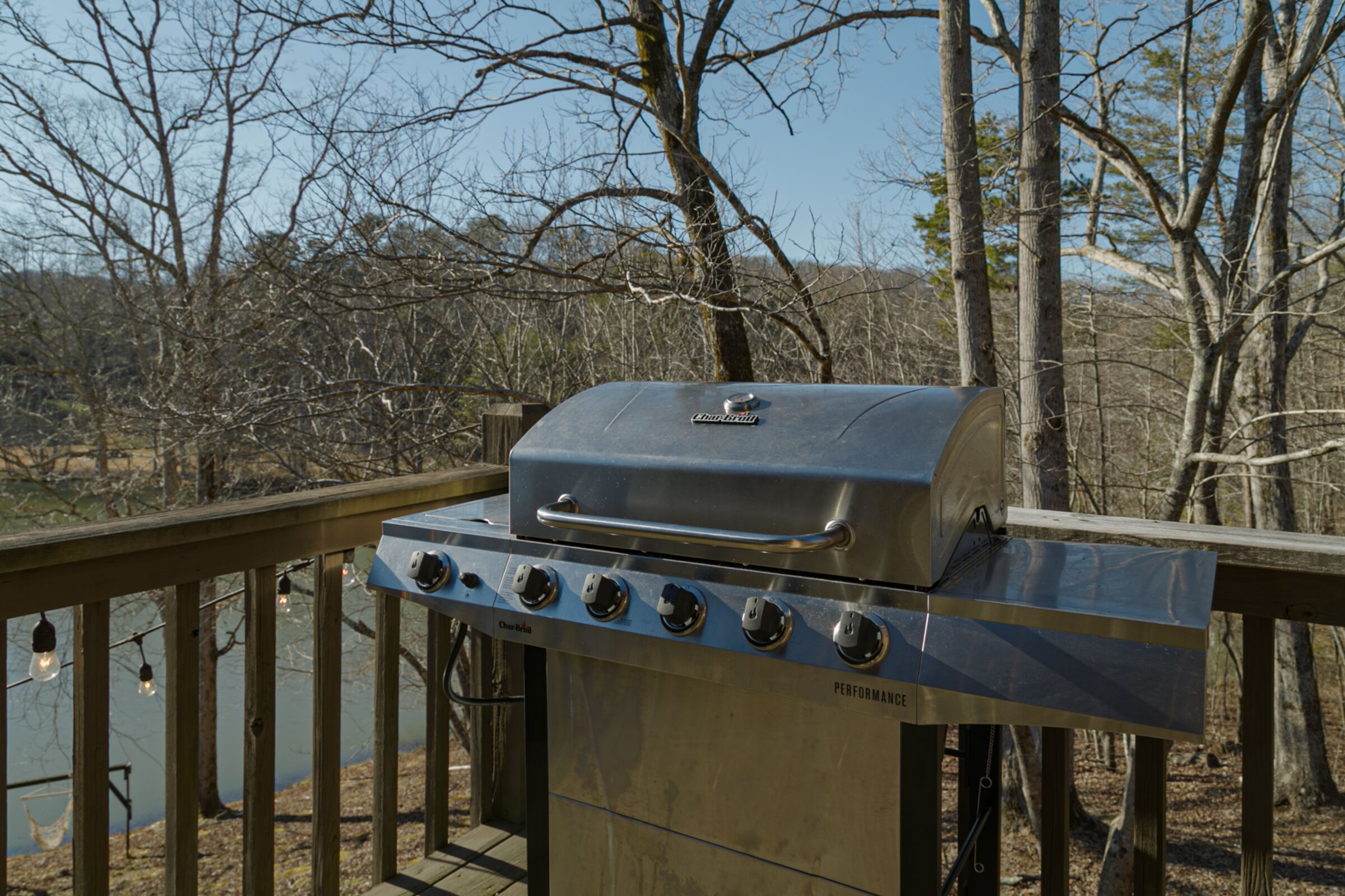 Una parrilla de gas portátil con cuatro quemadores y una tapa, ubicada sobre una terraza de madera con barandilla.