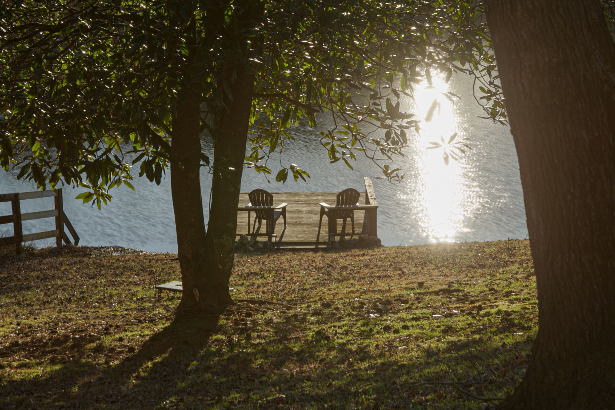 Un cadre idyllique au bord du lac, avec une jetée en bois, deux chaises et une table placées sous un arbre.