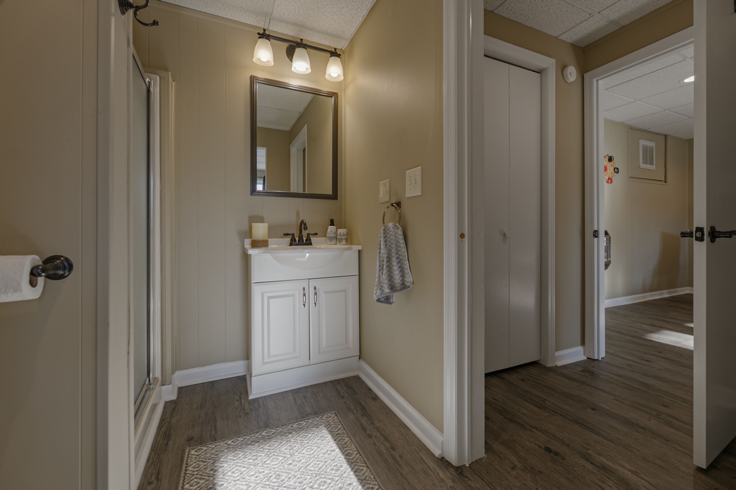 A bathroom with a white vanity, a large mirror, and a wooden floor.