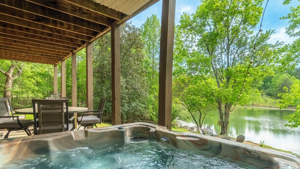 A hot tub area with a wooden pergola, surrounded by lush greenery and a lake view. - Wine Country Lake Escape-Fishing and Hot tub (Cleveland)