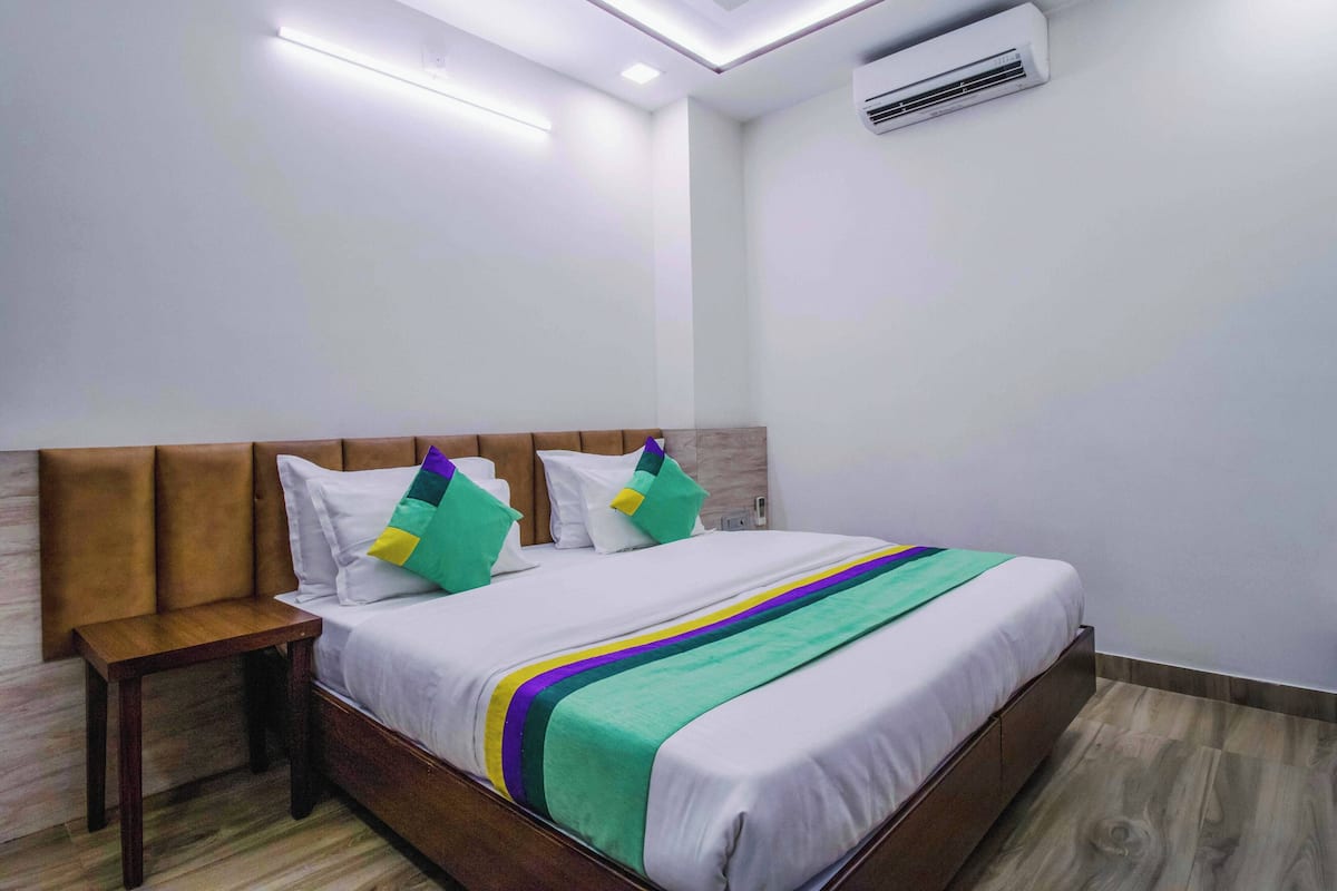 A neatly made bed with a wooden headboard, a bedside table, and an air conditioning unit on the wall.