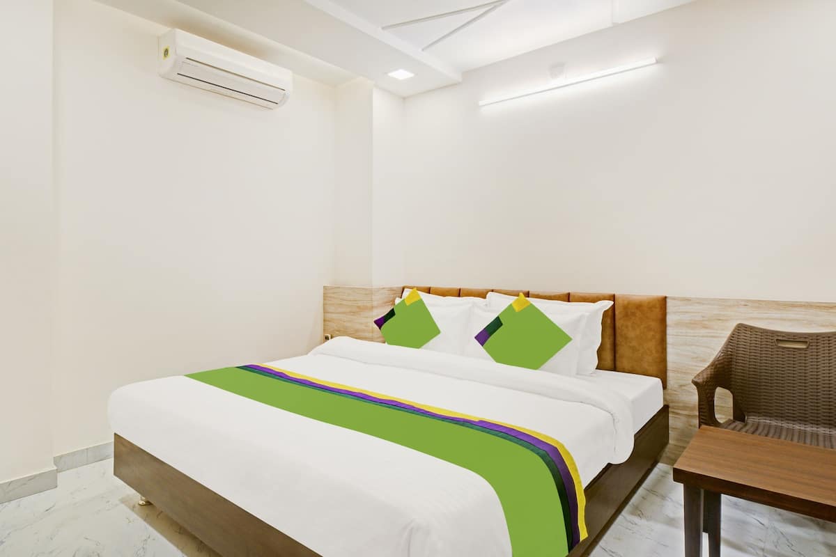 A hotel room with a bed, a chair, a table, and an air conditioning unit.