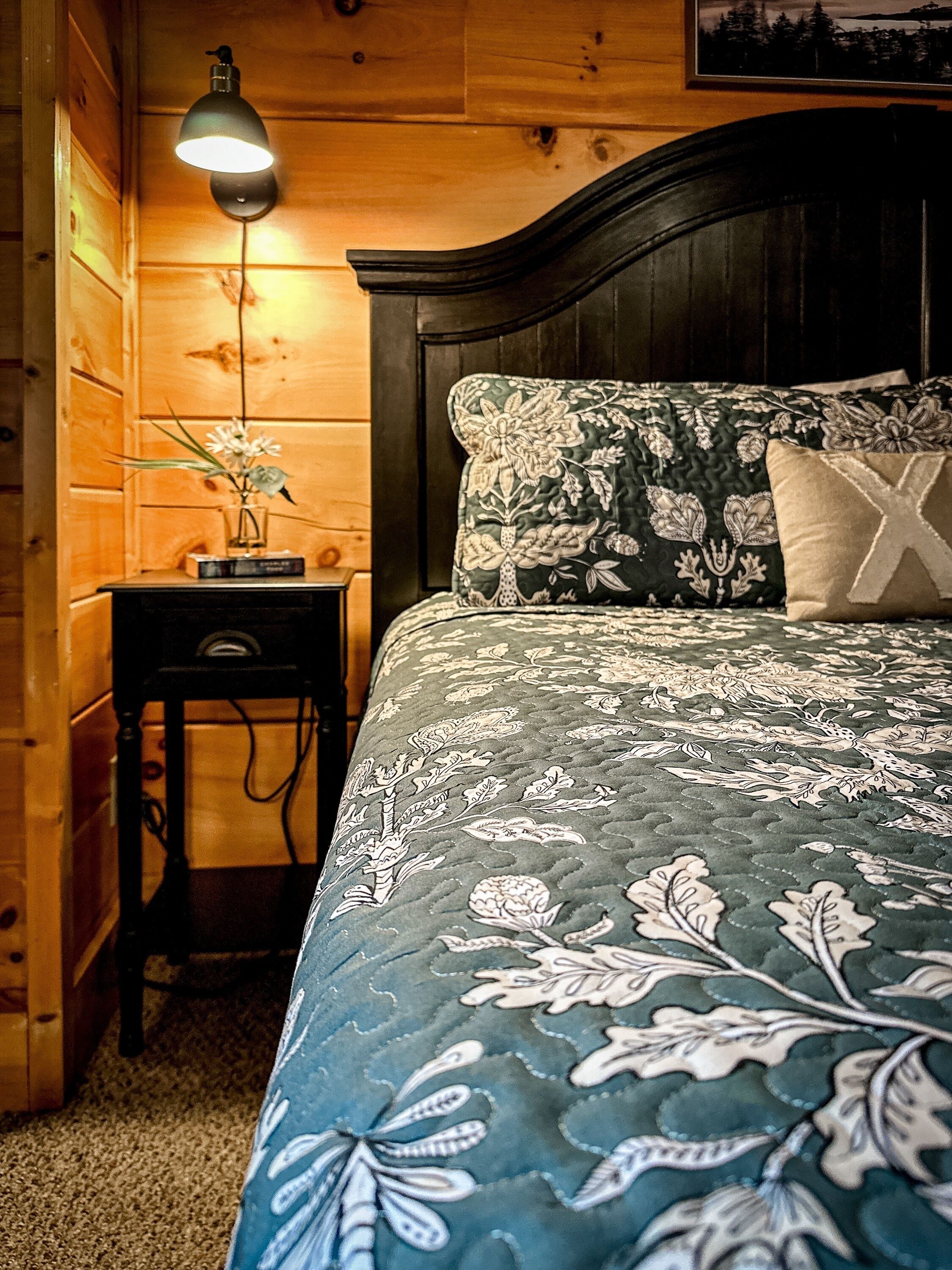 A wooden cabin bedroom with a bed, a nightstand, a lamp, and a framed picture on the wall.