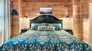 A wooden cabin bedroom with a bed, a headboard, a nightstand, a lamp, and a framed picture on the wall. - Mountain View/Hot Tubs/Pools/Game Room/Putt-Putt Course/Master Bedrooms (Sevierville)