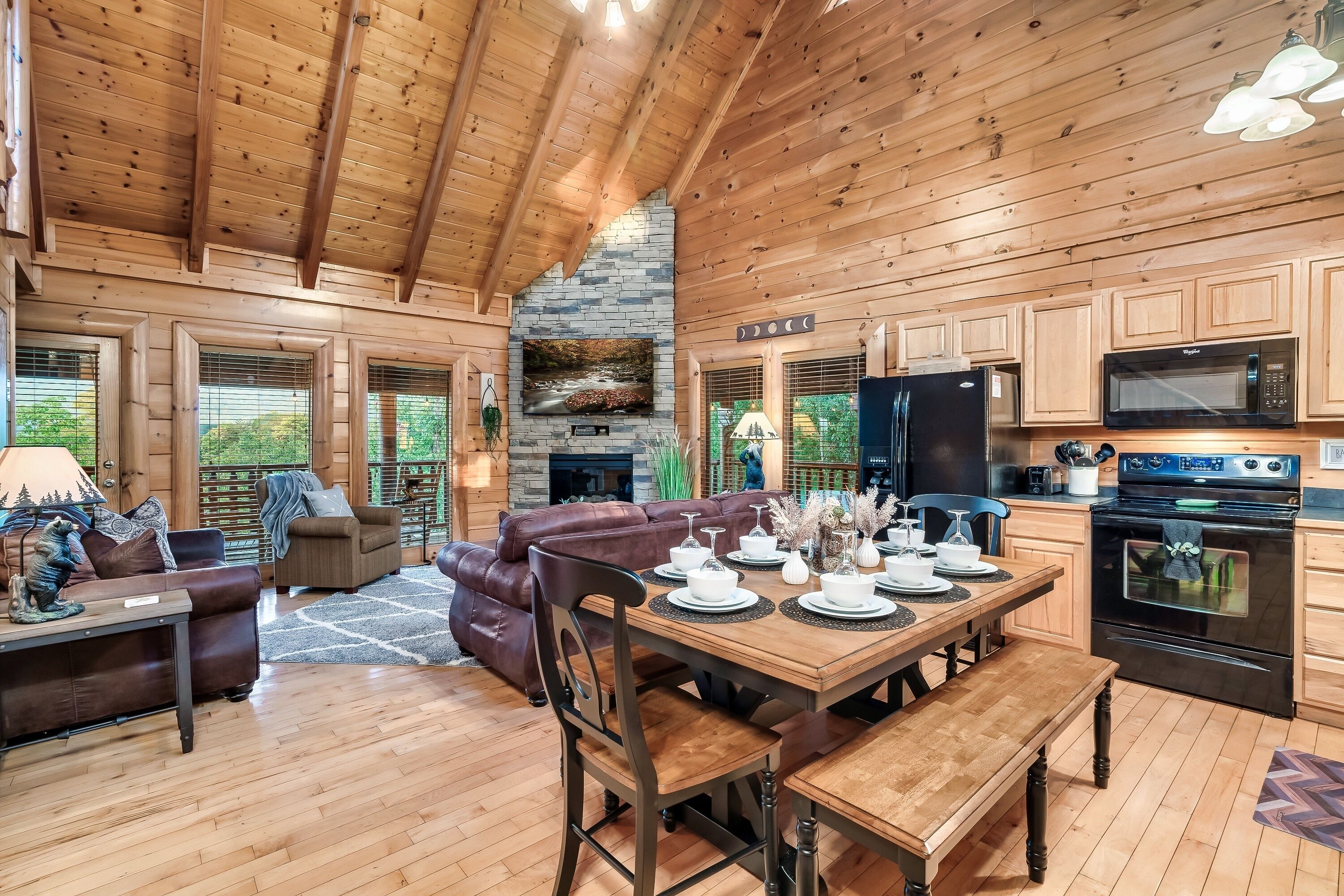 Un intérieur de chalet chaleureux avec un coin repas, un plafond en bois, une cheminée en pierre et des appareils de cuisine modernes.