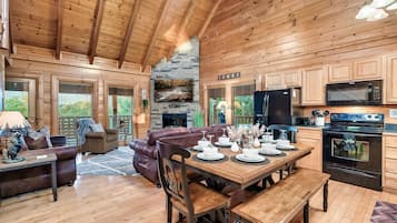 Un intérieur de chalet chaleureux avec un coin repas, un plafond en bois, une cheminée en pierre et des appareils de cuisine modernes.