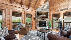 A cozy log cabin interior with a stone fireplace, wooden walls, and a comfortable seating area. - Mountain View/Hot Tubs/Pools/Game Room/Putt-Putt Course/Master Bedrooms (Sevierville)