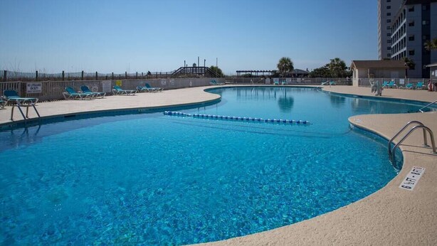 Ein klares, blaues Schwimmbecken mit Liegestühlen und einem Rettungsschwimmerstand.