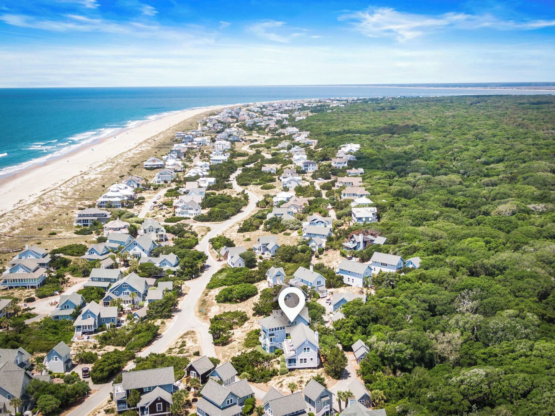 A coastal residential area with houses along the beach and dense greenery inland.