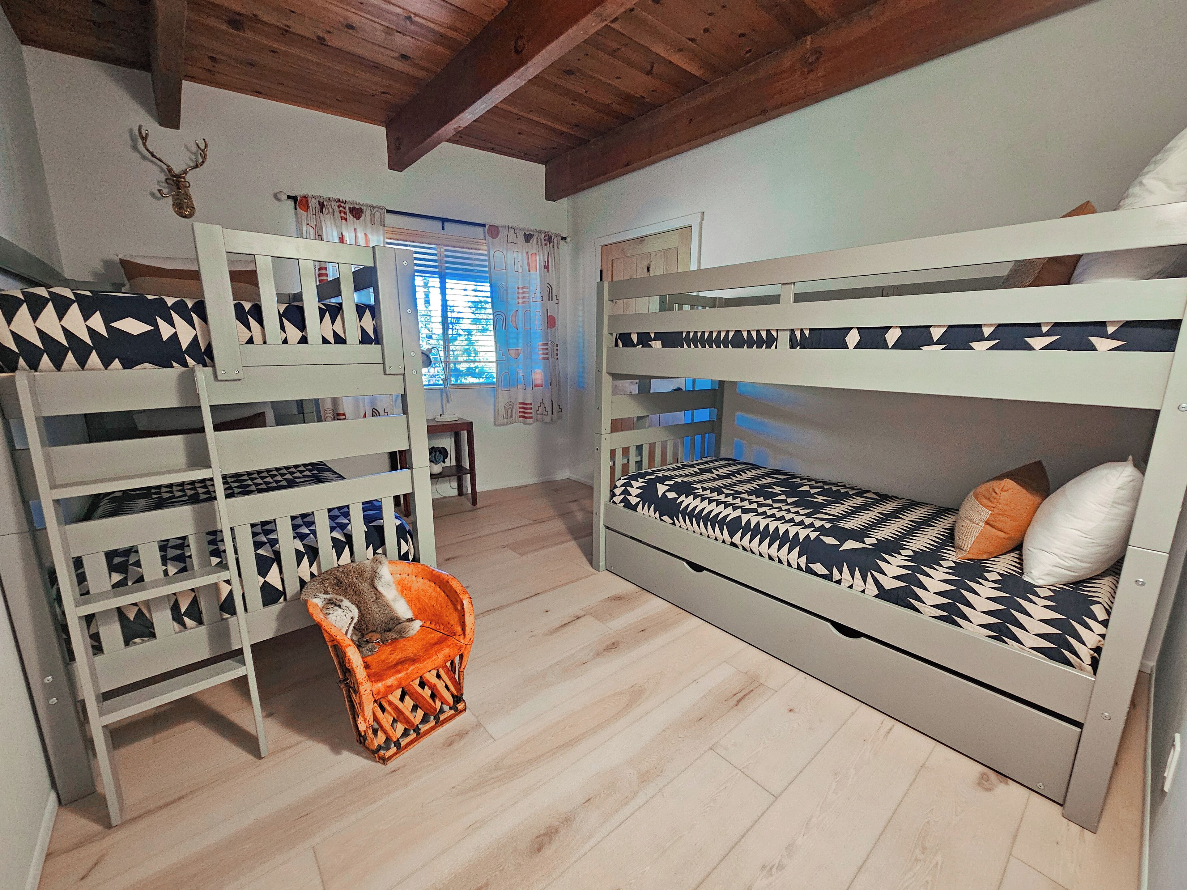 Una habitación con literas, techo de madera y una ventana con cortinas.