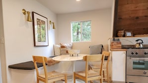 Een gezellige keuken met een ronde tafel, houten stoelen, een fornuis en een raam met uitzicht op bomen.