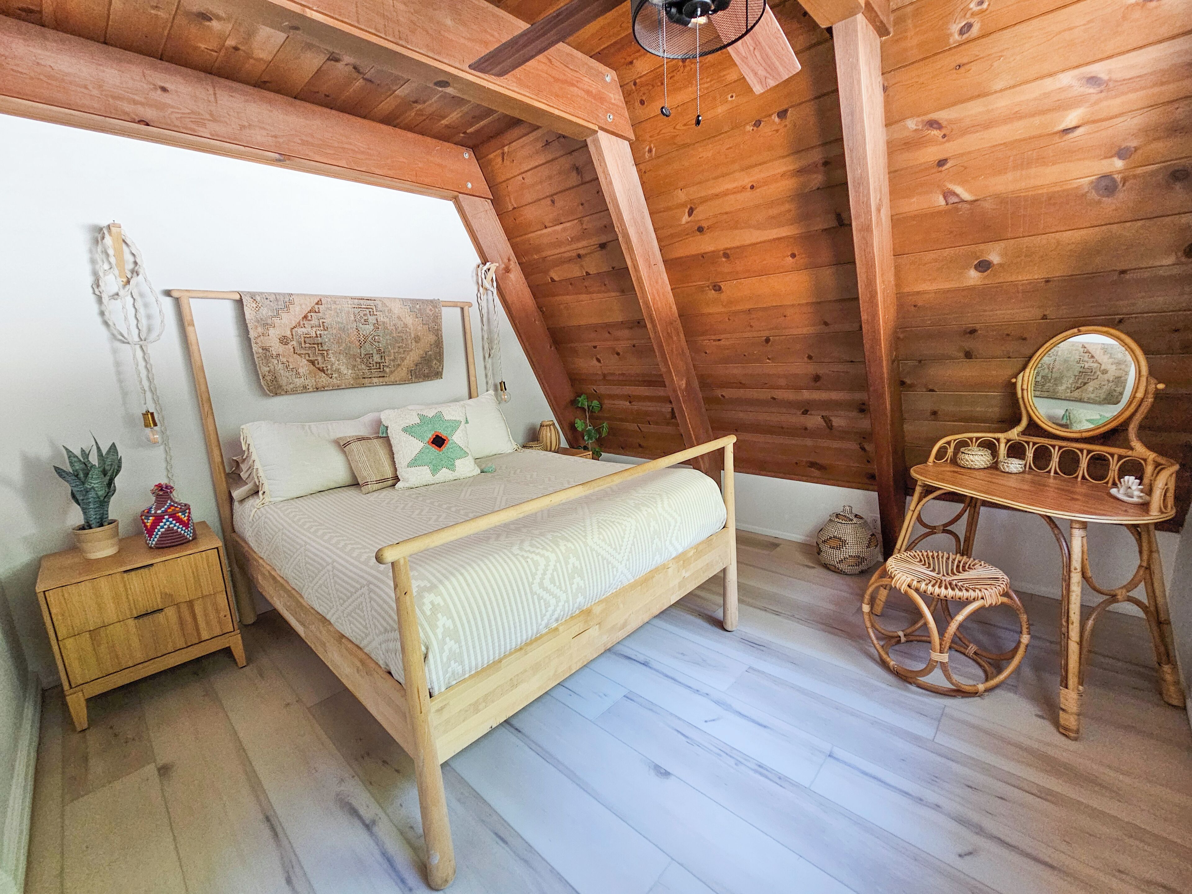 A cozy attic bedroom with a wooden bed, a small bedside table, a wicker chair, and a mirror.