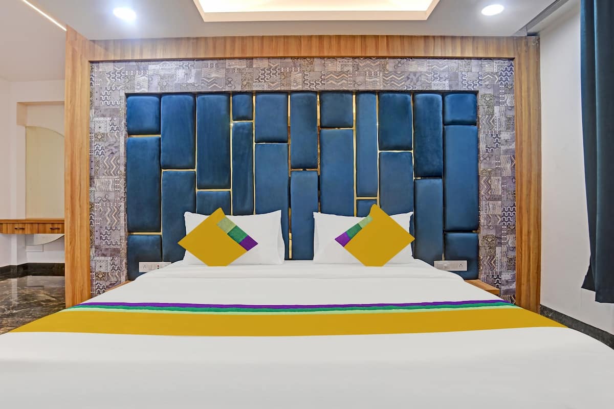 Una habitación de hotel con una cama grande, cabecera de madera, baldosas de pared estampadas y suelo de mármol.