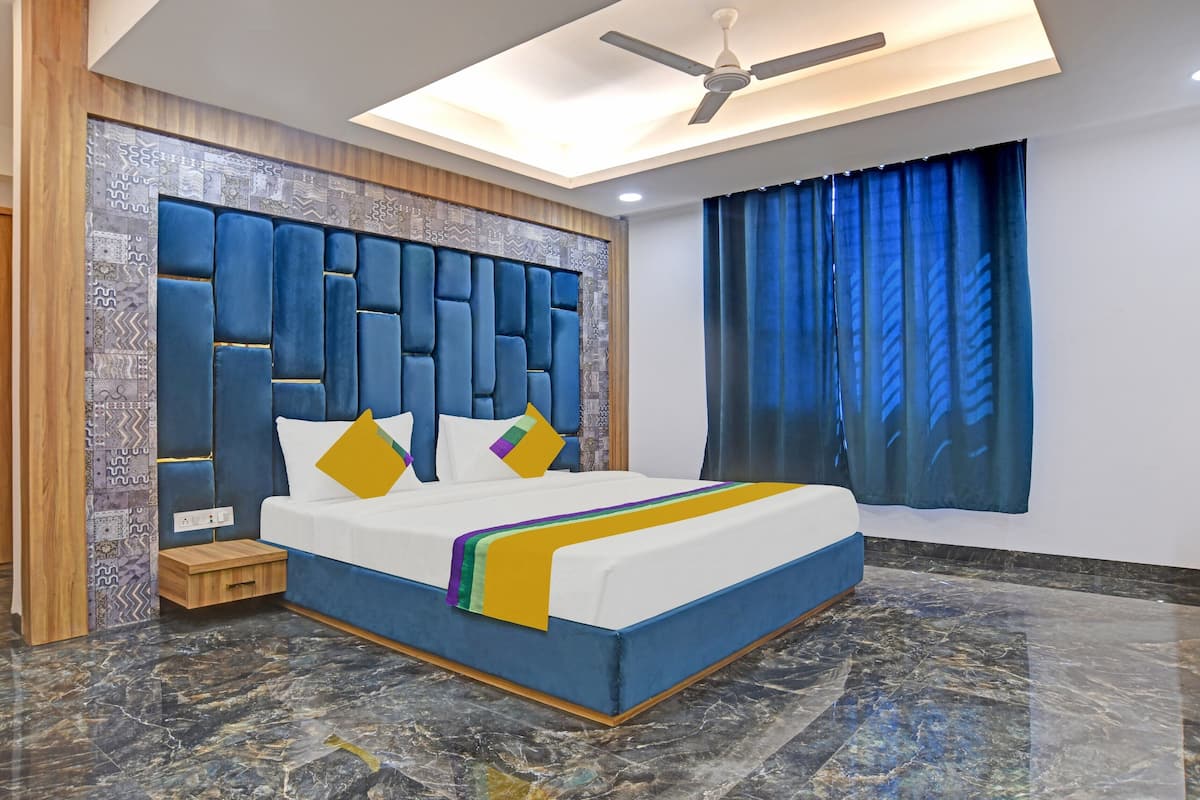 Una habitación de hotel moderna con una cama grande, un armario de madera, una mesita de noche pequeña de madera y un ventilador de techo.