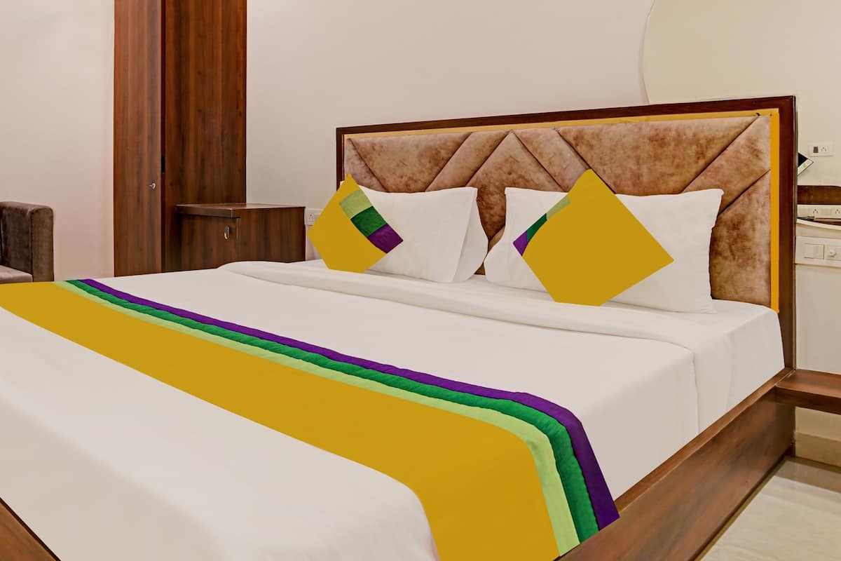 Una cama bien hecha con un edredón blanco, una manta a rayas de colores y dos almohadas con diseños geométricos.