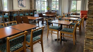 A restaurant with wooden tables and chairs, stone walls, and large windows. - The Addison Hotel, SureStay Collection by Best Western (Addison)