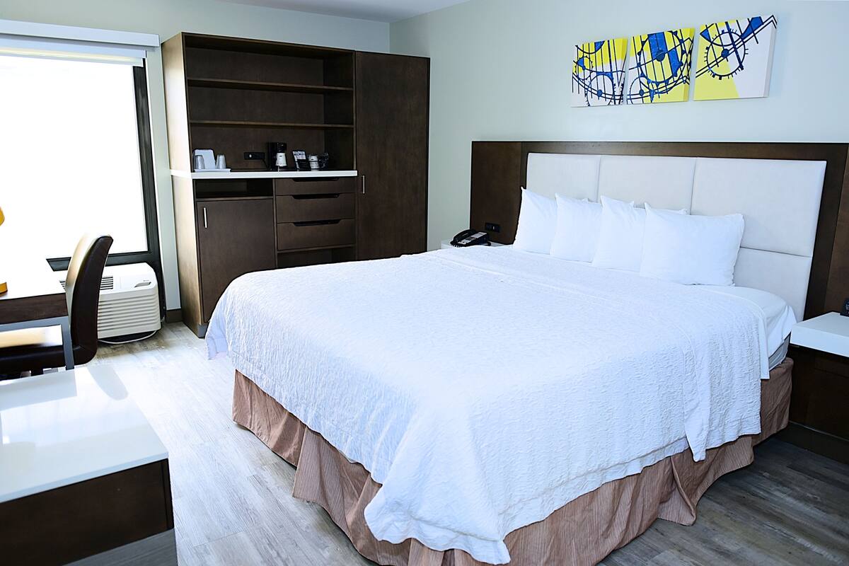 Une chambre d’hôtel avec un grand lit, un bureau avec une chaise, une armoire et une œuvre d ’art accrochée au mur.