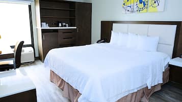 Habitación de hotel con una cama grande, un escritorio con silla, un armario y una obra de arte en la pared.