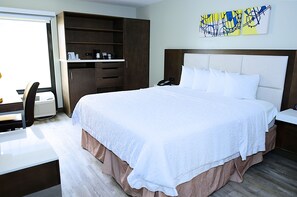 A hotel room with a large bed, a desk with a chair, a wardrobe, and a wall-mounted artwork.