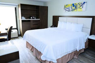 Habitación de hotel con una cama grande, un escritorio con silla, un armario y una obra de arte en la pared.
