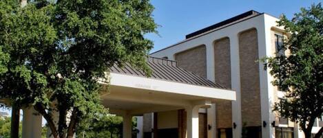 A hotel with a covered entrance, large windows, and a brick facade.
