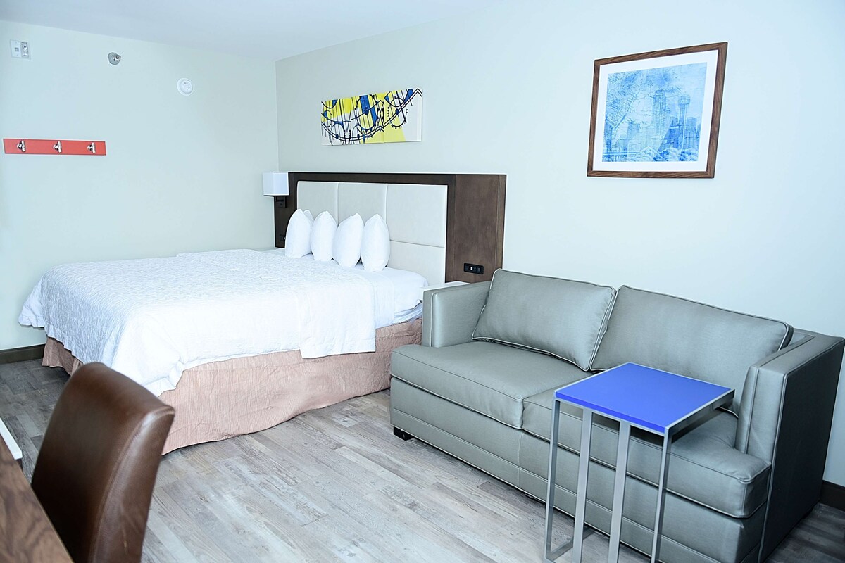Ein Hotelzimmer mit einem Bett, einem grauen Sofa, einem kleinen Tisch und einem Sessel.