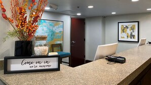 A reception area with a framed sign, a vase of dried branches, a painting, and a door. - The Addison Hotel, SureStay Collection by Best Western (Addison)