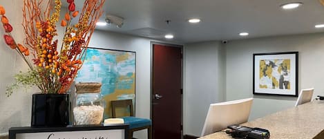 A reception area with a framed sign, a vase of dried branches, a painting, and a door.