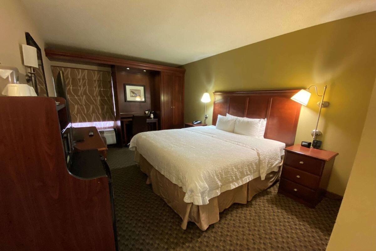 Une chambre d’hôtel avec un grand lit, un bureau, une chaise, une lampe et une commode.