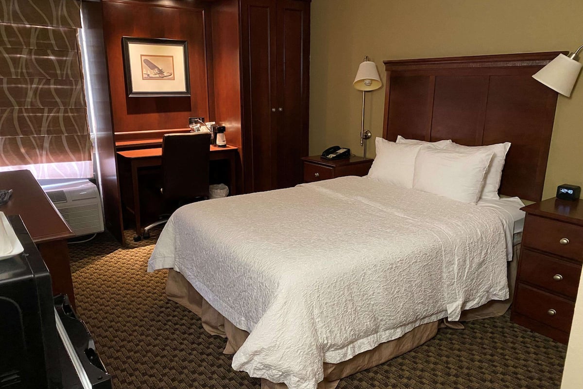 Une chambre d’hôtel avec un grand lit, un bureau, une chaise, une lampe et une horloge.