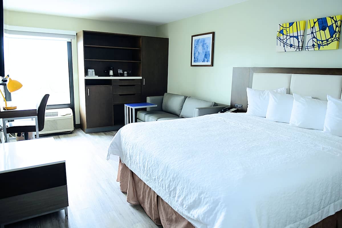 Une chambre d’hôtel avec un grand lit, un bureau avec une chaise, un canapé, une armoire et un tableau au mur.