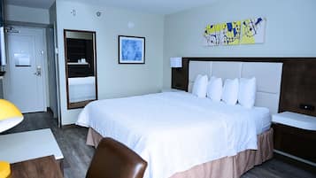 Habitación de hotel con una cama grande, una mesita de noche, una silla, un escritorio, un espejo y obras de arte en la pared.