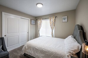 Une chambre à coucher avec un lit, une chaise, une porte et une fenêtre avec des rideaux.